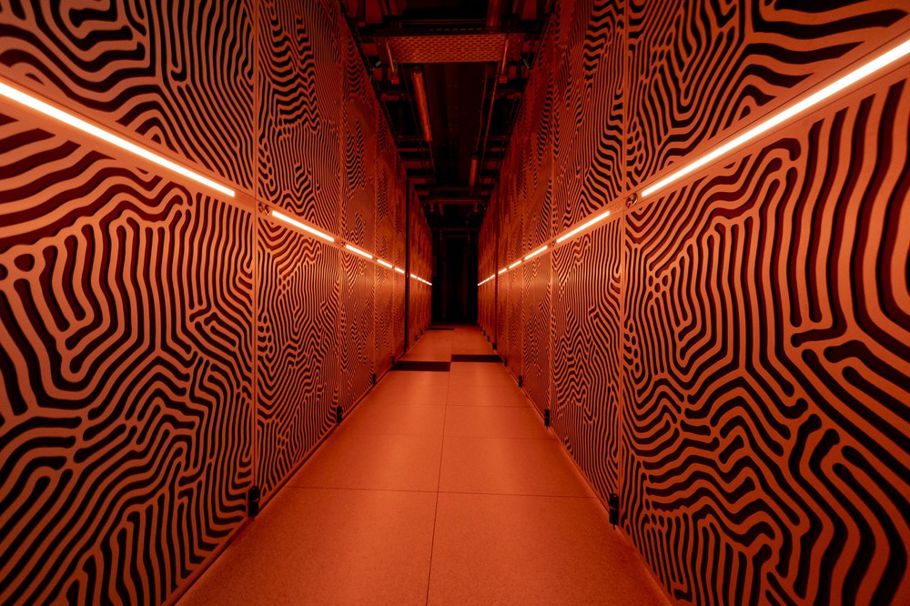 Geschlossene Supercomputer-Schränke von Jupiter am JSC (Jülich Supercomputing Centre) mit markanten schwarz-weißen organischen Mustern, die von rot-orangefarbener Beleuchtung erhellt werden und einen futuristischen, korridorartigen Effekt erzeugen.
