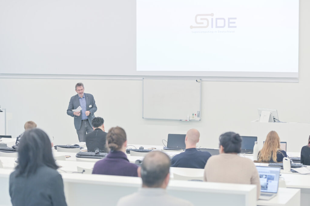 Dr. Andreas Wierse steht vorne im hellen Hörsaal des HLRS und spricht zu den Teilnehmenden, die in Reihen sitzen und auf Laptops arbeiten. Auf der Leinwand ist das SIDE-Logo zu sehen.